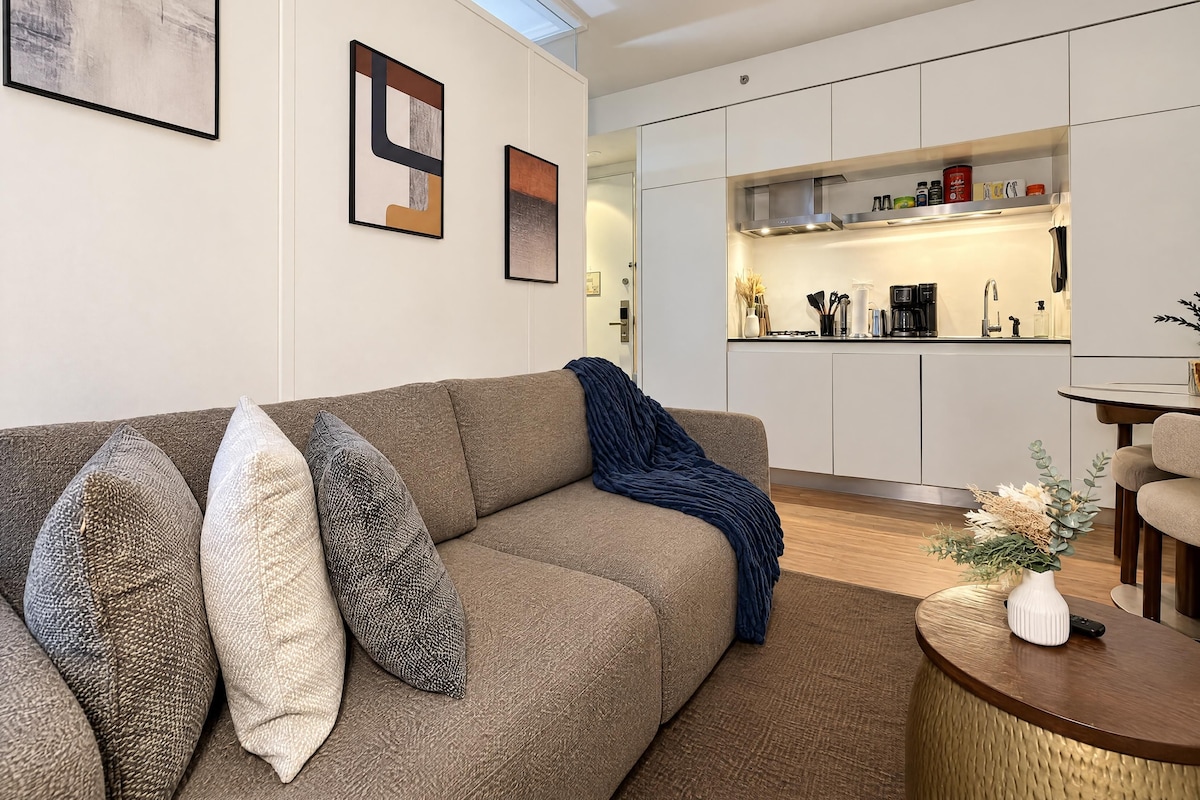 Una sala de estar moderna con un sofá, almohadones, una mesa de centro y una cocina al fondo.