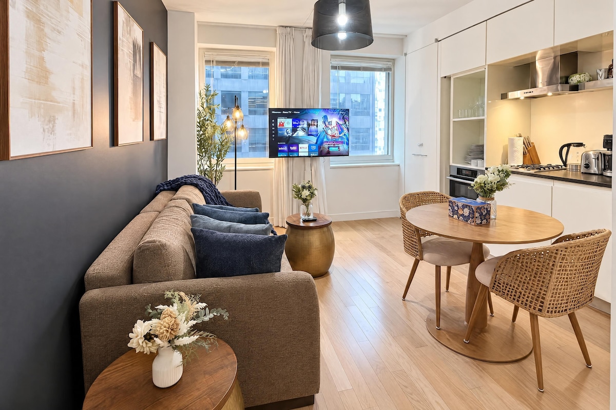 Una sala de estar moderna con un sofá, una mesa de comedor con sillas, un televisor y una zona de cocina.