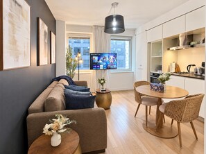 A modern living room with a sofa, a dining table with chairs, a TV, and a kitchen area.