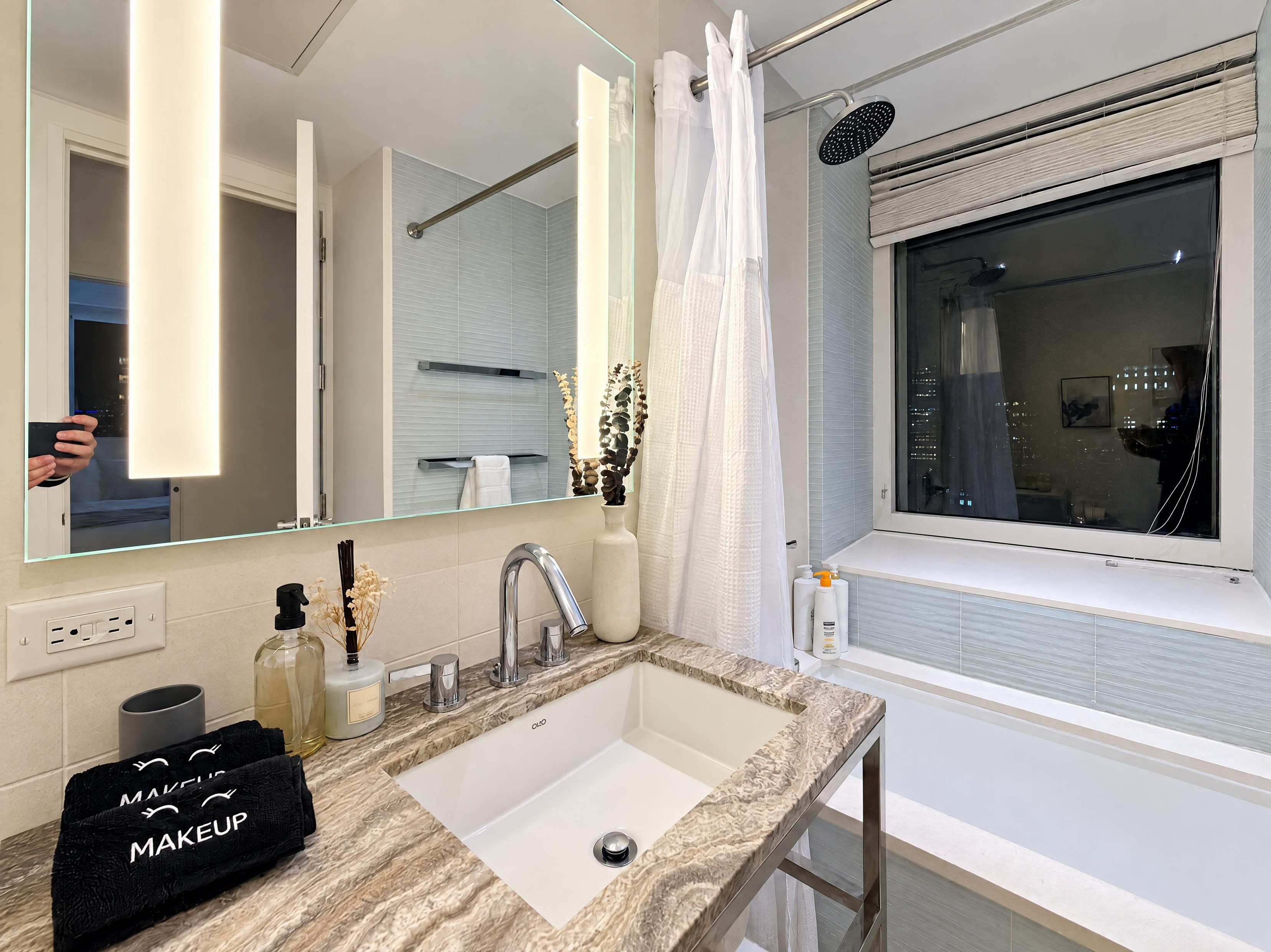 A modern bathroom with a large mirror, a bathtub, and a vanity with a sink.