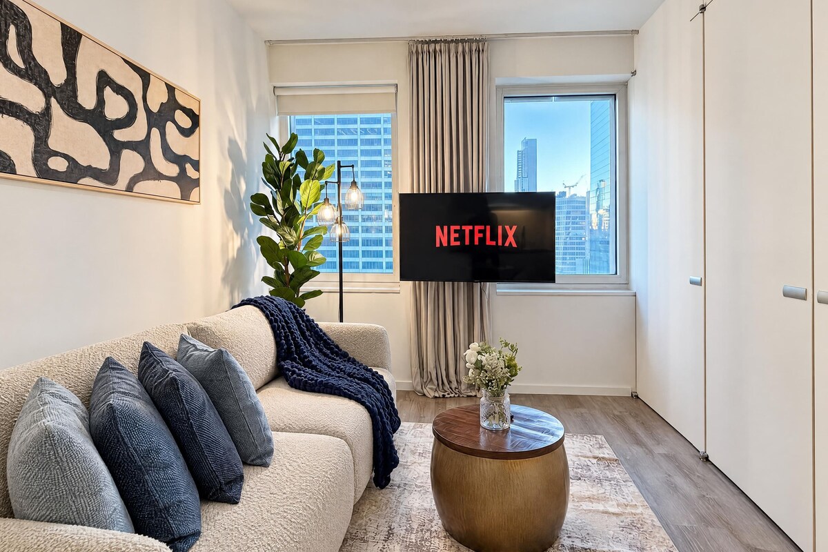 A modern living room with a beige sofa, a round coffee table, and a large TV screen displaying 'NETFLIX'.