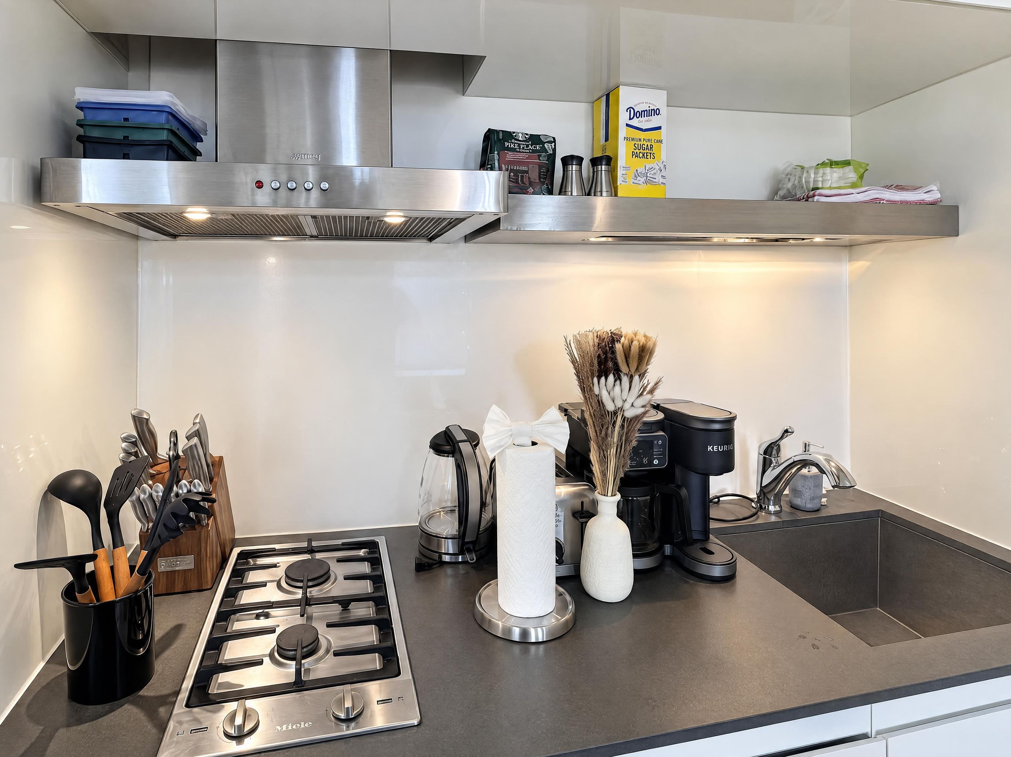 A modern kitchen with a stainless steel range hood, a coffee maker, and a box of Domino sugar packets.