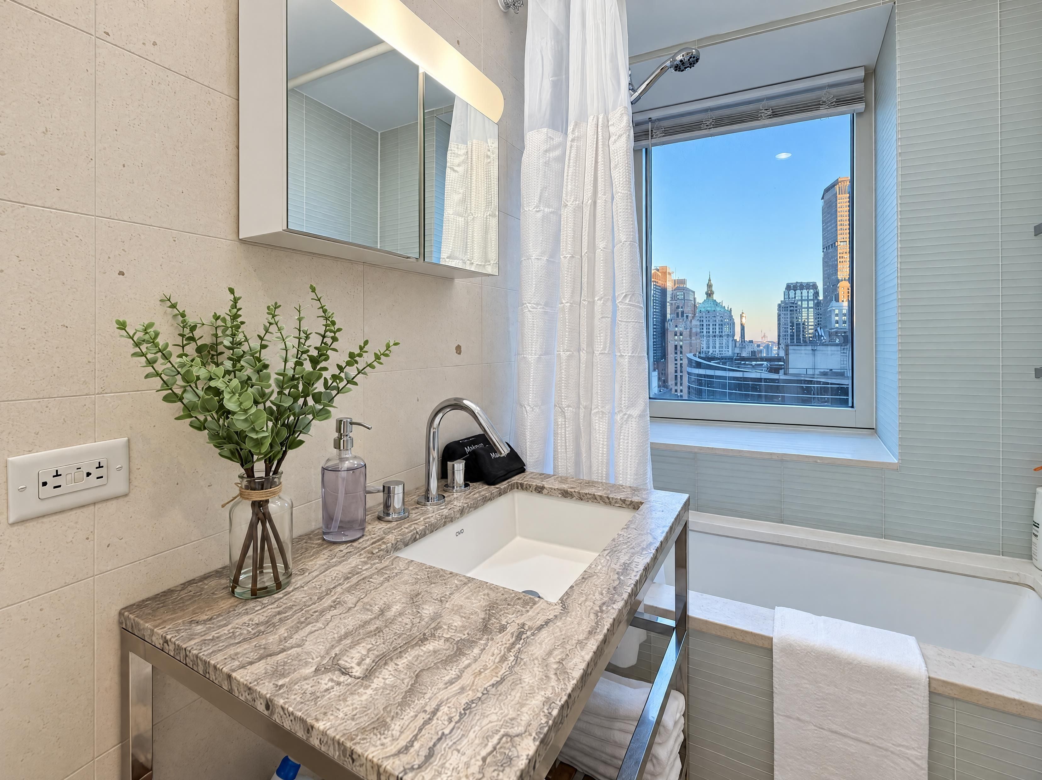 Ein modernes Badezimmer mit Marmorplatte, einem großen Spiegel, einer Duschkabine und Blick auf die Stadt.