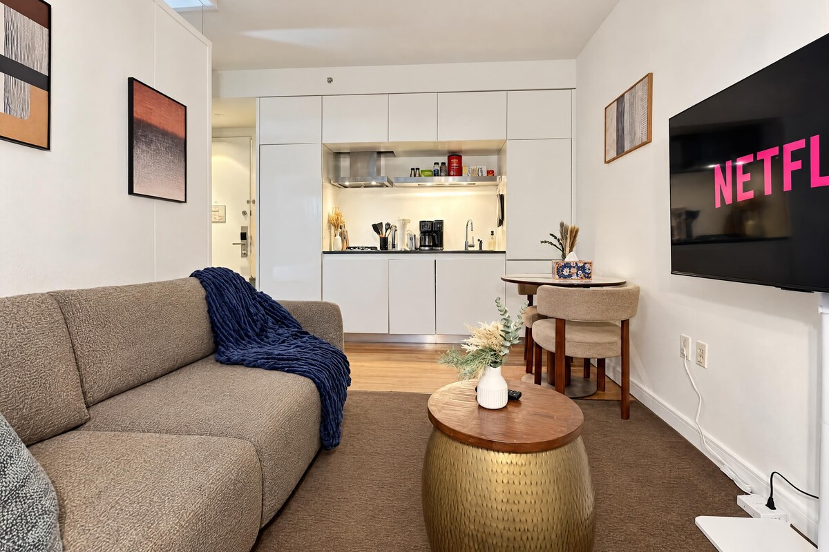A modern living room with a sofa, a coffee table, a TV, and a kitchen in the background.