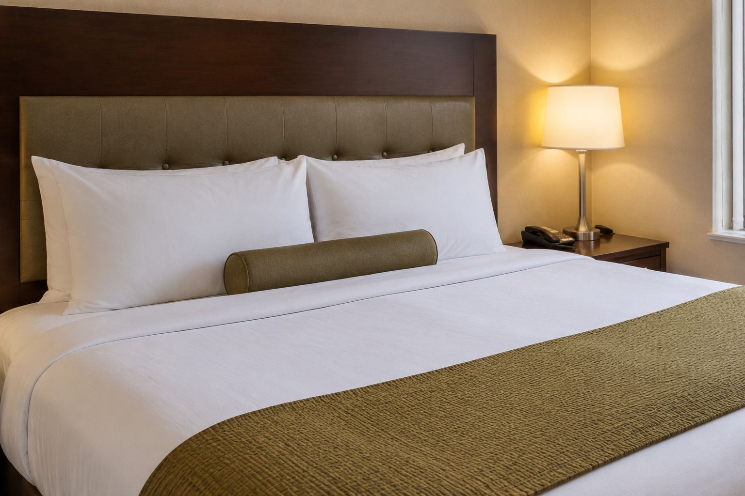 Ein Hotelzimmer mit Bett, Kopfteil, Nachttischlampe und Nachtschränkchen.