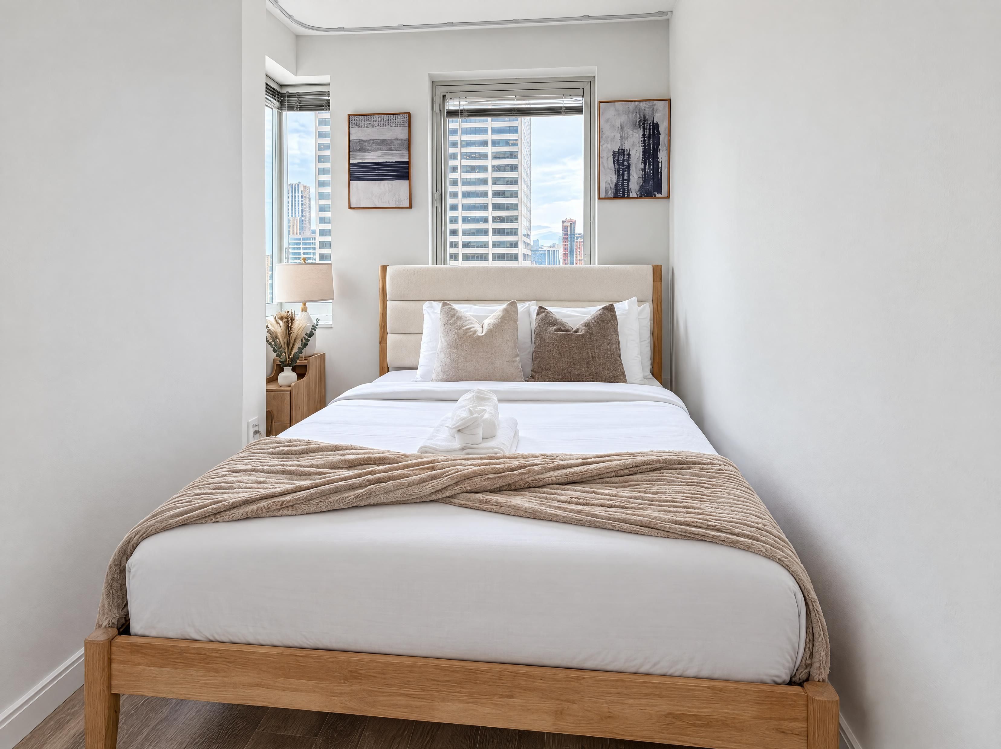 A modern bedroom with a large bed, a nightstand with a lamp, and two framed artworks on the wall.