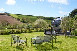 A garden with two metal chairs, a wooden deck, and a spherical structure. - Valley cottage with hot tub (Kingsbridge)