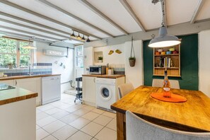 A kitchen with a wooden table, a washing machine, and a microwave. - Valley cottage with hot tub (Kingsbridge)