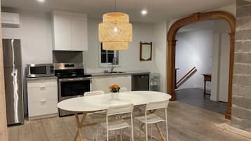 A modern kitchen with stainless steel appliances, a white dining table with chairs, and a hanging light fixture.