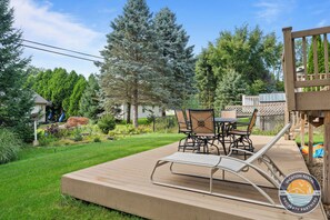 Eine Holzterrasse mit Tisch und Stühlen, umgeben von einem Garten mit verschiedenen Pflanzen und Bäumen.