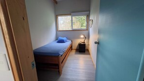 A narrow room with a bed, a nightstand, and a window.