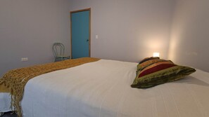 A bedroom with a bed, a chair, a door, and a wall socket.