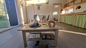 Moderni keittiö, jossa on ruokailutila, suuri ikkuna sekä puinen pöytä, jonka päällä on kirjoja ja vedenkeitin.
