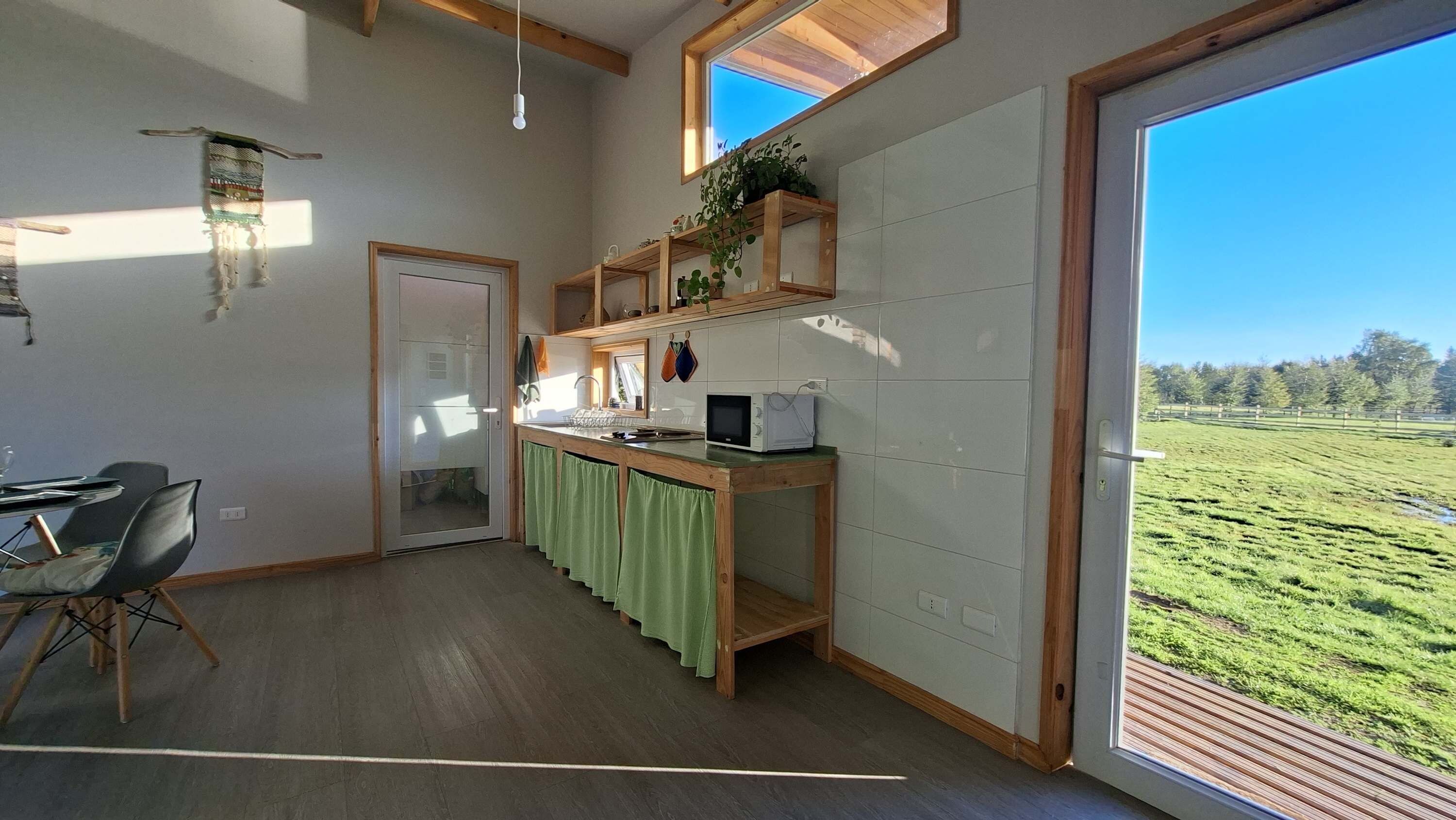 Une cuisine dotée d’un plan de travail en bois, d’un four à micro-ondes et offrant une vue sur un champ verdoyant grâce à une grande fenêtre.