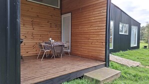 Eine Holzterrasse mit Tisch und Stühlen, einer Tür und einem kleinen Gartenbereich.