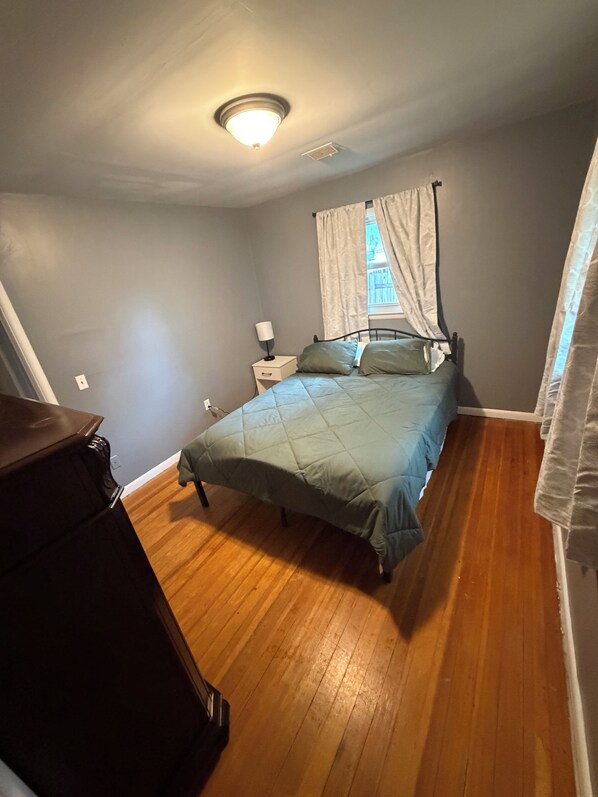 Un dormitorio con cama, mesita de noche, lámpara y ventana con cortinas.