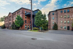 Straßenansicht mit zwei Backsteingebäuden, eines mit blauer Fassade und das andere mit roter Fassade. Vor den Gebäuden stehen Bäume und der Himmel ist klar.