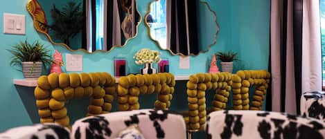 Una habitación con paredes color turquesa, dos espejos grandes con marcos dorados, una consola blanca con un florero y un sofá con estampado blanco y negro.