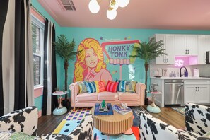 Un salon chaleureux et accueillant, avec un canapé rose, un tapis aux couleurs vives et une fresque murale.