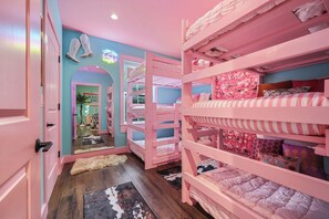 Ein zartrosa eingerichtetes Schlafzimmer mit Etagenbetten, einem Spiegel und einem Neon-Leuchtschild.