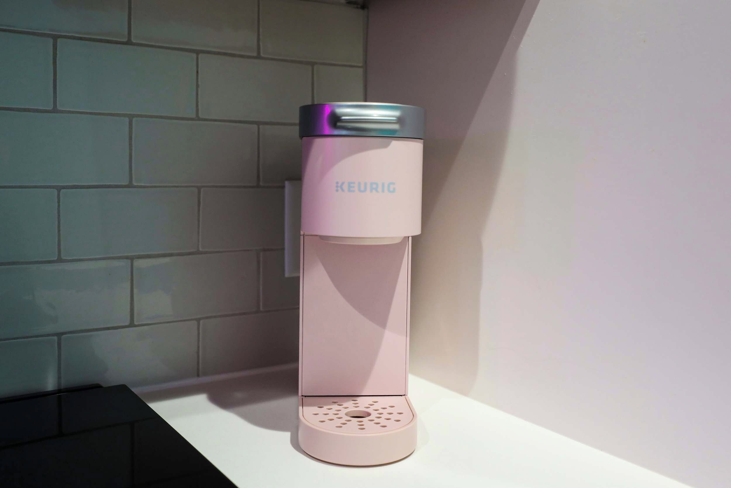 Een KEURIG koffieapparaat op een wit aanrecht tegen een betegelde muur.