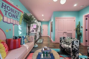 A vibrant living room with a pink sofa, a patterned armchair, and a wall mural. - Pink Cowgirl Pad · Sleeps 6 · Midtown Nashville (Nashville)