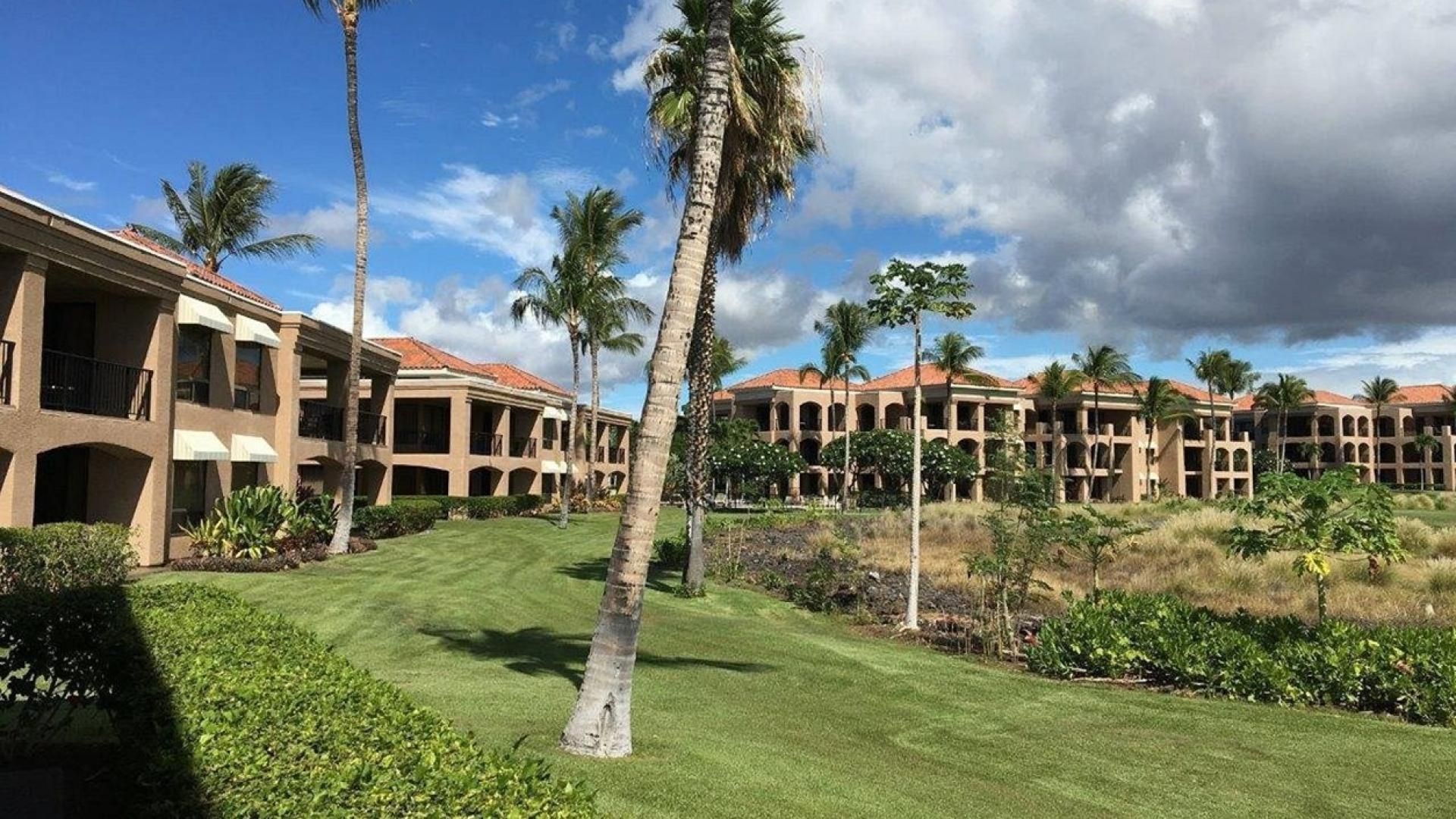 A hotel with multiple-story buildings, a well-maintained lawn, and palm trees.