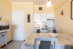 A compact kitchen with white cabinets, a built-in oven, and a dining area with a patterned tablecloth. - Studio Apartment Zeedijk With Ocean View (Blankenberge)