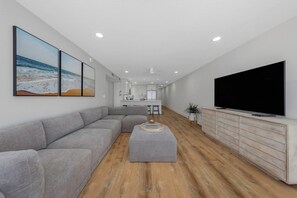 Een moderne woonkamer met een grijze hoekbank, een flatscreen televisie en een houten vloer.