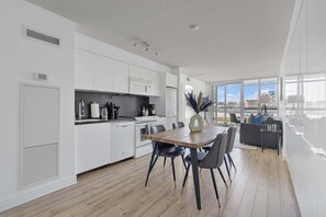 A modern kitchen with white cabinets, a dining area with a wooden table and chairs, and a large window offering a view of the city. - Sleek Downtown Oasis  Modern Retreat in Toronto | Parking Available (Toronto)