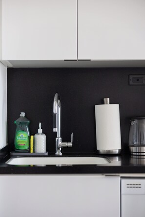 A kitchen with a sink, a dish soap bottle, a paper towel dispenser, and a glass pitcher. - Sleek Downtown Oasis  Modern Retreat in Toronto | Parking Available (Toronto)