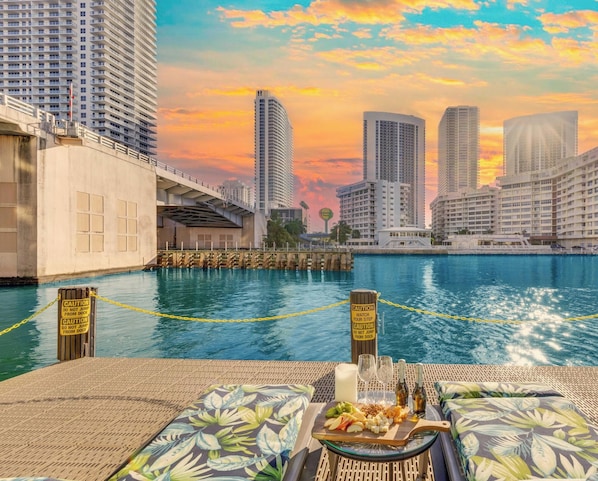 A waterfront dining area with a view of the city skyline, a dock, and caution signs. - Beachwalk Pininfarina Studio, Pool & Beach Shuttle (Hallandale Beach)