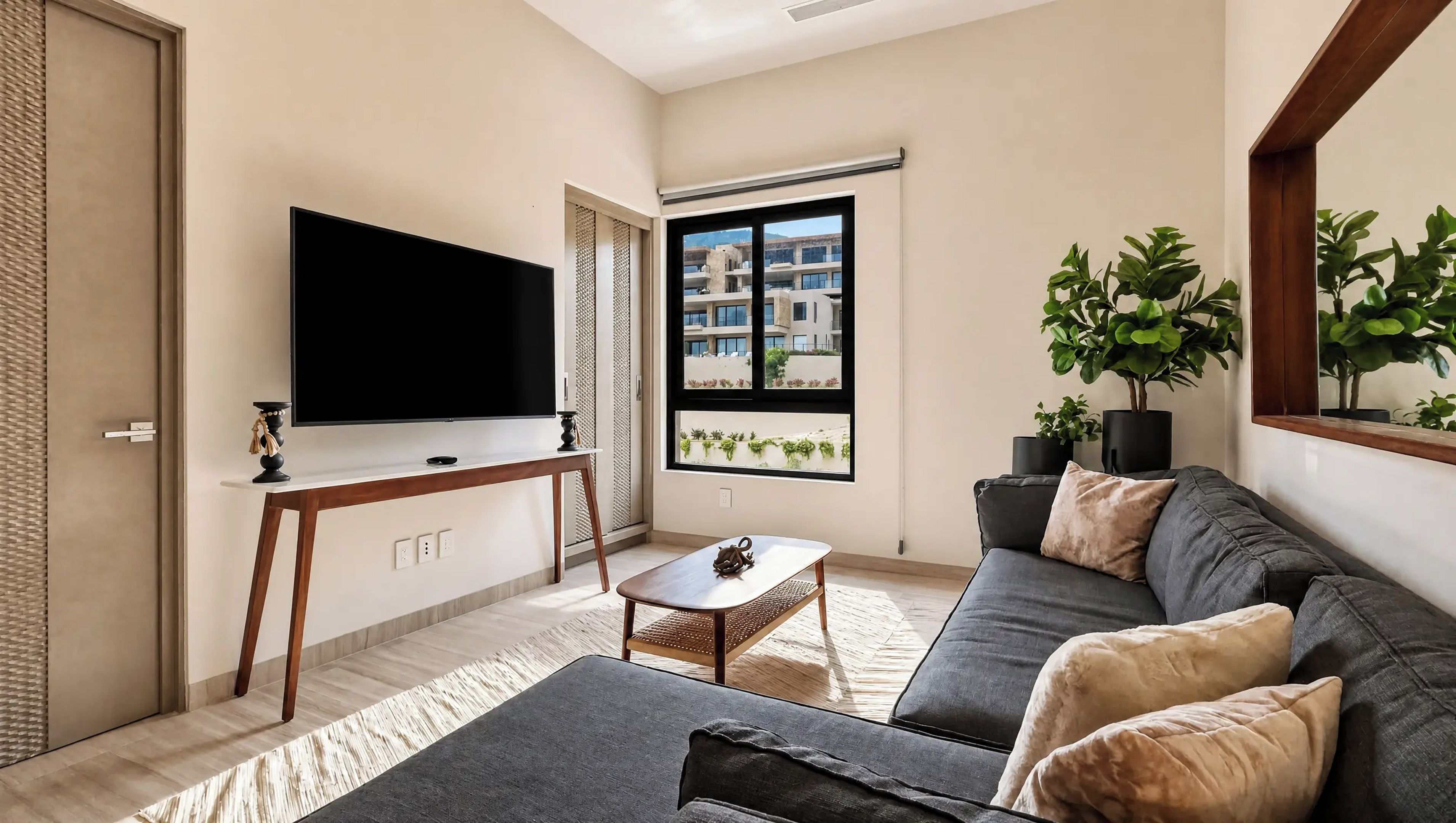 A modern living room with a flat-screen TV, a sofa, a coffee table, and a large window with a view of buildings.