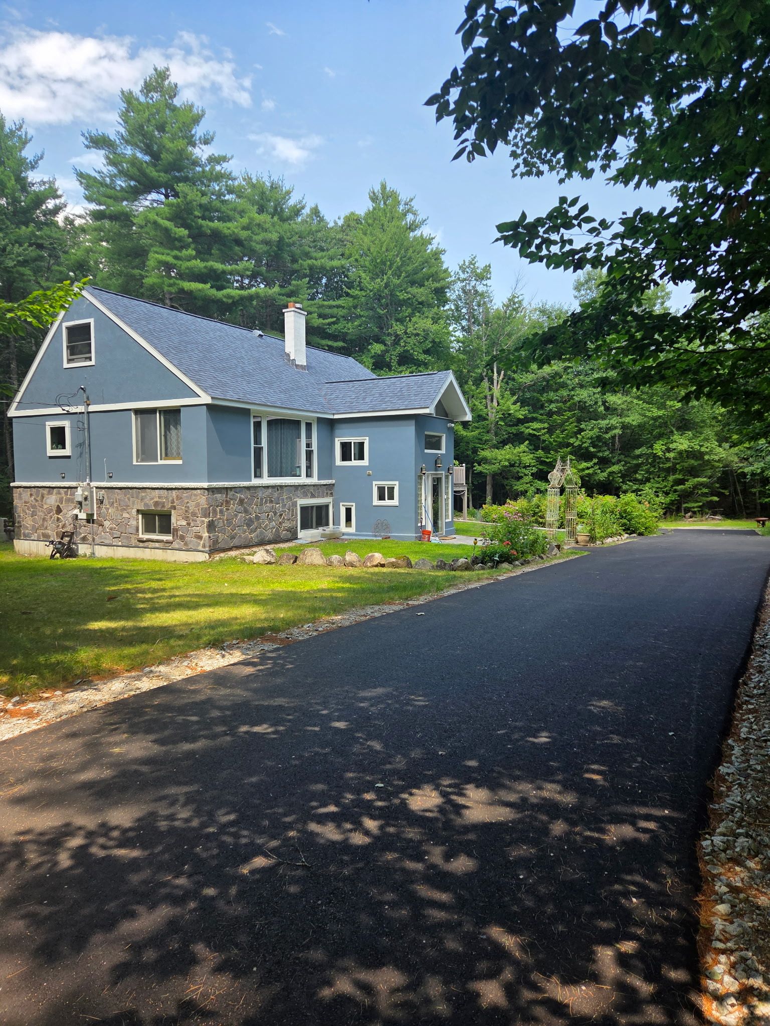 A two-story house with a stone foundation, a sloped roof, and a front porch.