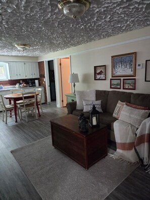 A living room with a wooden coffee table, a sofa, and a lamp. There is a kitchen in the background with cabinets and a countertop. - Adorable 1-bedroom apartment in Conway perfect for your getaway (Conway)