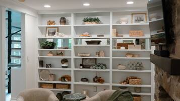 A cozy living room with a fireplace, a bookshelf filled with decorative items, two armchairs, and a coffee table.