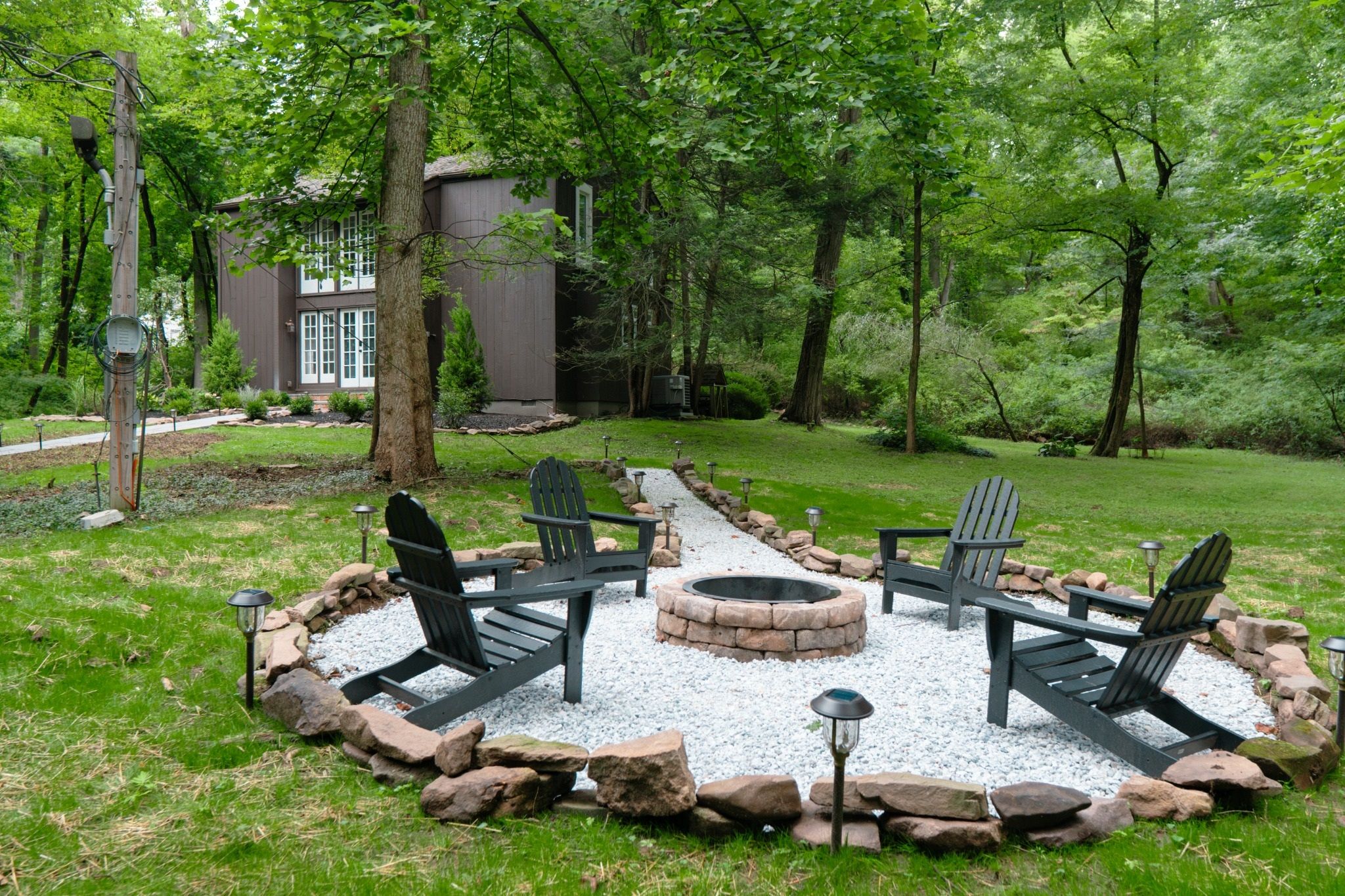 A circular outdoor seating area with Adirondack chairs and a fire pit, surrounded by a stone border.