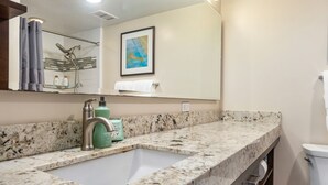 Une salle de bain avec un comptoir en granit, un lavabo, une douche avec une porte en verre, un tableau encadré au mur et un porte-serviettes.