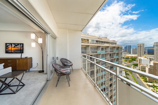 Ein Balkon mit Blick auf eine Stadtansicht, eine Couch, ein Sessel und ein Gemälde.