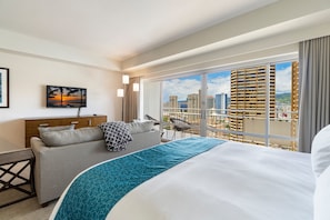 Ein Hotelzimmer mit Bett, einer Couch, einem Fernseher, Blick auf die Stadt und einem Balkon.
