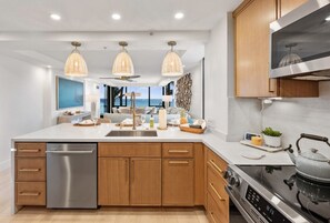 A modern kitchen with wooden cabinets, a stainless steel dishwasher, a gas stove, and pendant lighting. - Mahana #311 New Oceanfront Corner Remodel - 2 bed/2 bath (Lahaina)