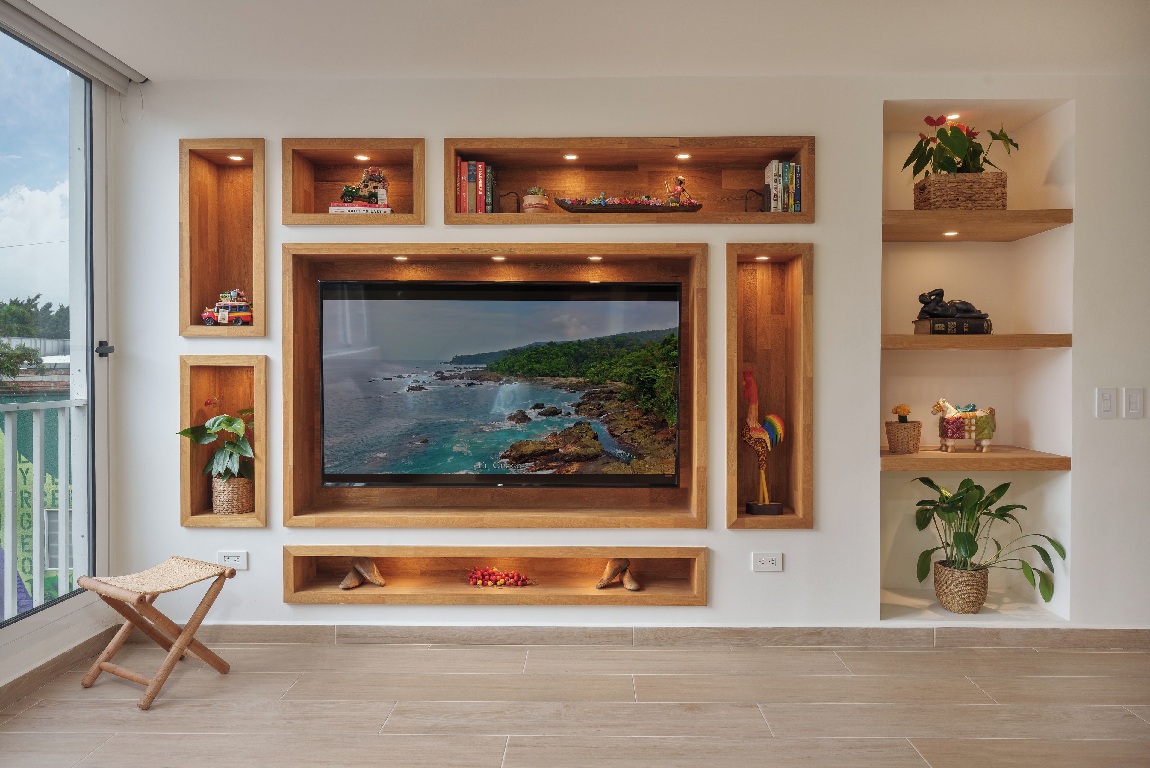 A living room with a large flat-screen TV mounted on a wooden wall, surrounded by shelves with books and decorative items.