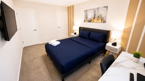 Habitación de hotel con cama, mesitas de noche, escritorio, silla, televisor y un cuadro en la pared.