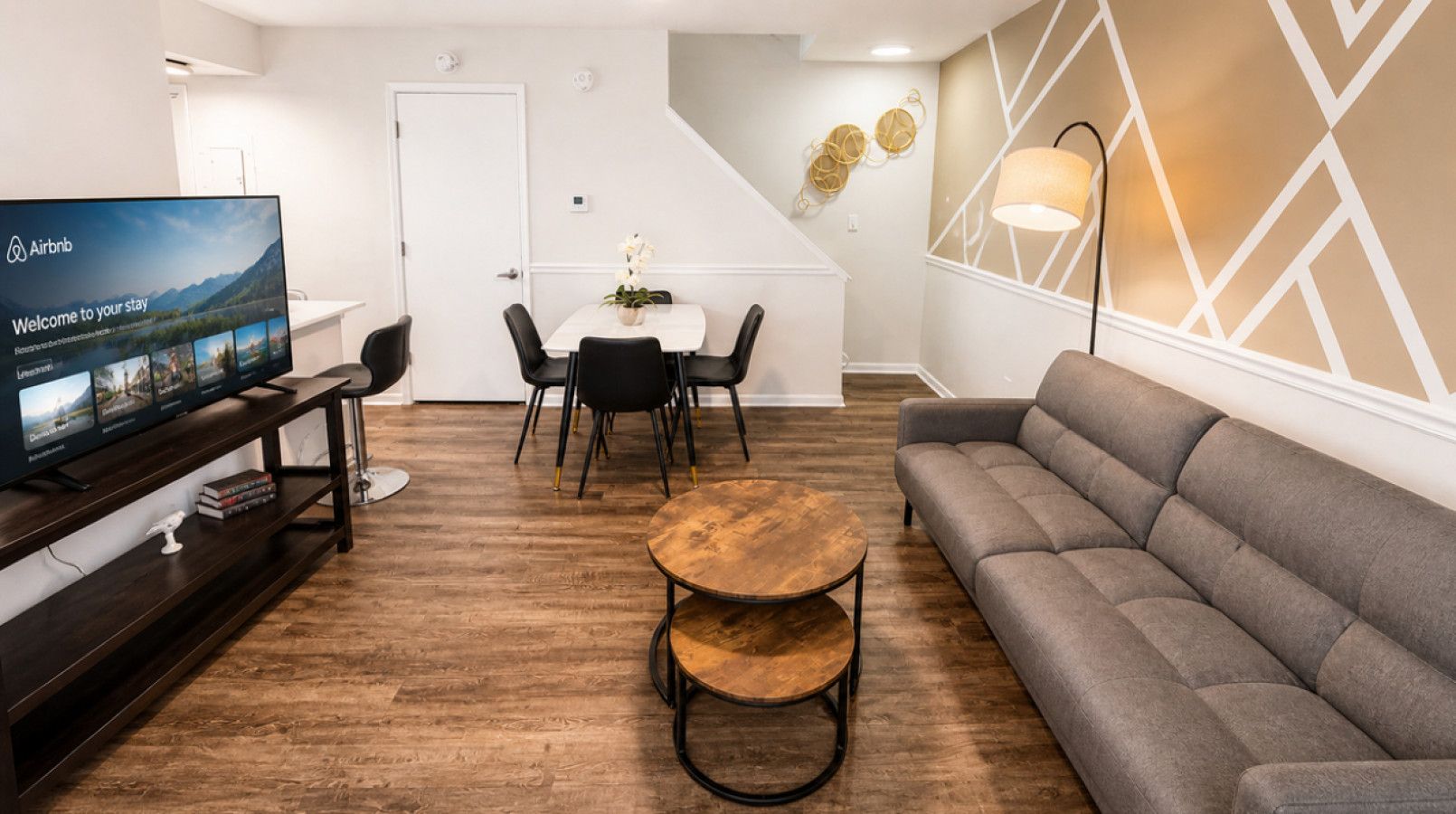 Ein modernes Wohnzimmer mit Flachbildfernseher, einer Couch, einem runden Couchtisch und einem Essbereich mit Stühlen und einem Tisch.