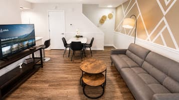 Ein modernes Wohnzimmer mit Flachbildfernseher, einer Couch, einem runden Couchtisch und einem Essbereich mit Stühlen und einem Tisch.