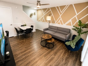 Una sala moderna con un sofá gris, una mesa de centro redonda y un sillón azul.