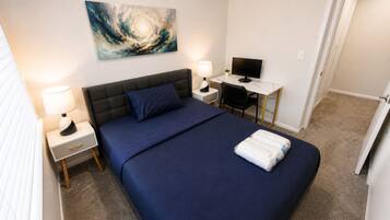 A bedroom with a bed, two bedside tables with lamps, a desk with a computer, and a painting on the wall.