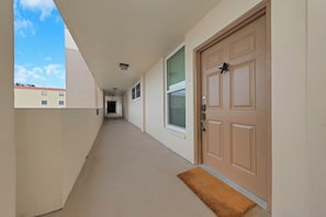 A corridor with a door at the end, a window on the right, and a view of buildings outside. - Tranquil 2-bedroom condo in Madeira Beach 503 (Madeira Beach)