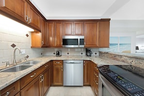 A modern kitchen with wooden cabinets, stainless steel appliances, and a granite countertop. - Tranquil 2-bedroom condo in Madeira Beach 503 (Madeira Beach)
