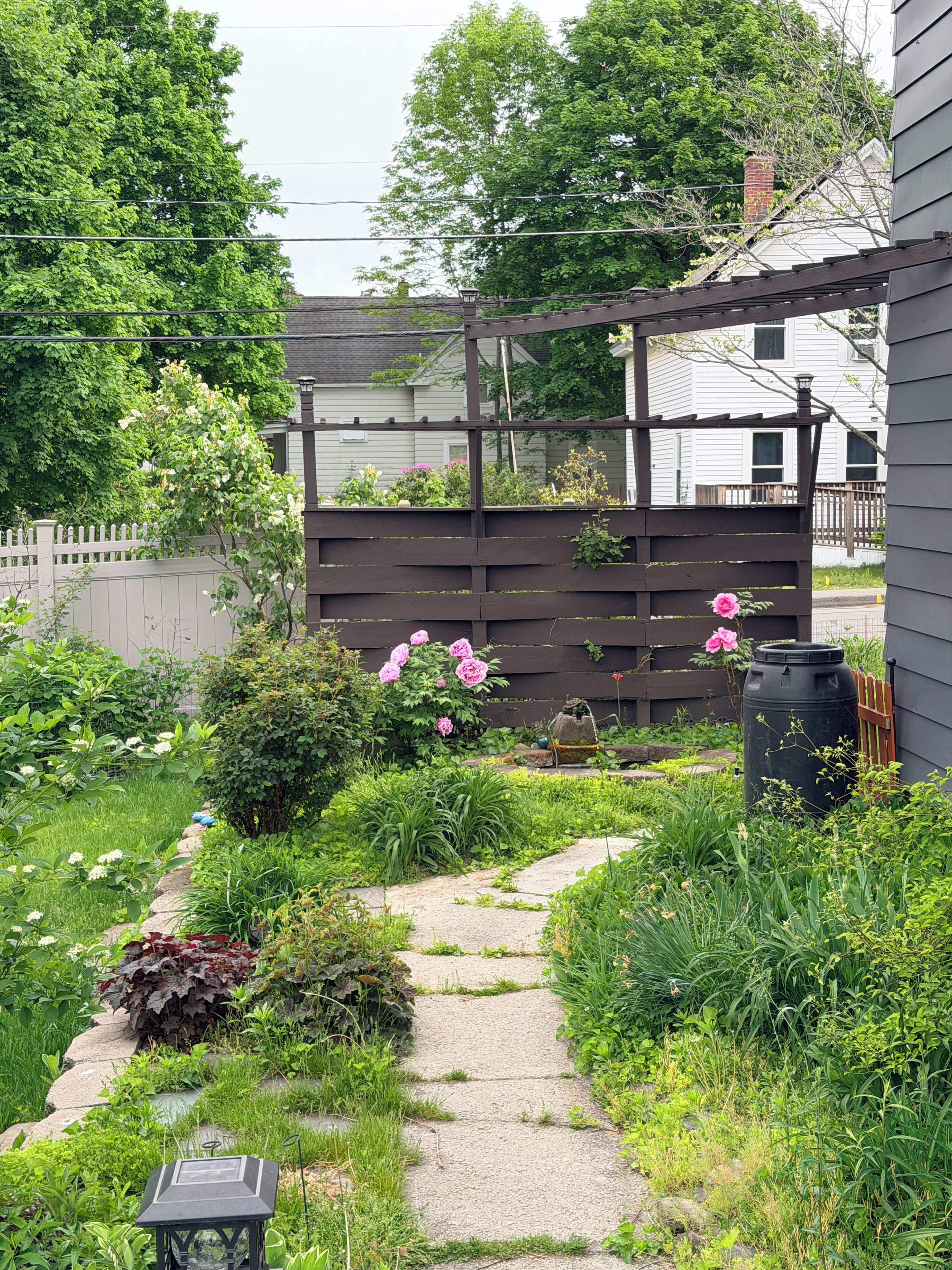 A garden with a stone pathway, a wooden fence, and various plants.